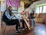 two girls play the flute either side of a young man playing the harp.