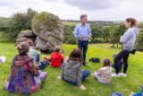 a guide gives a tour to a group of people who are sitting around a large boulder