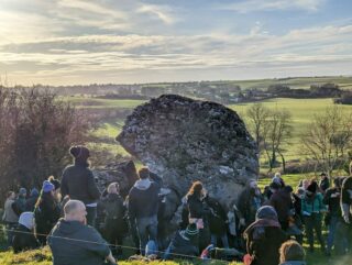 the large stone, with crowds of people surrounding it on a tour