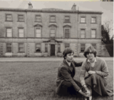 A man and lady sit on a lawn in front of Oldbridge House