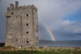 close view of the exterior of the castle, overlooking the sea, and a rainbow appearing from behind the castle.