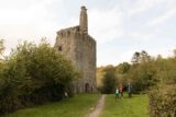 a square castle in the middle of the woods, with people standing outside looking at it.
