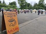 A board advertising a coffee stall with a market in the distance