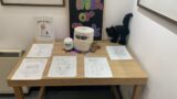 A table with sheets of art and some Halloween decorations