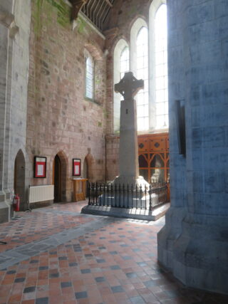 the cross standing within a section of a church, lit by a multi-paned window
