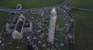 aerial view of the abbey complex, with roofless church, round tower, and graves.