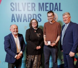 Four people stand in front a backdrop