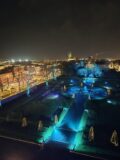 Aerial view of lit up Rose Garden with city buildings in the background,