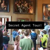 Children stand in a room of paintings with clip boards.
