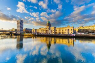 the custom house under a blue sky, which is reflected in the water in front of the building.