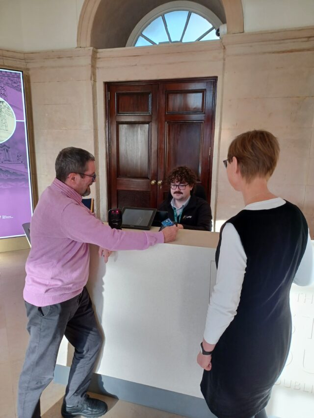 two people at a desk talking to the person behind the till
