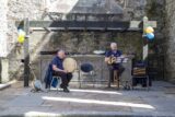 A man plays a bodhran while another sits to his left with a guitar