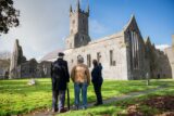 Three people stand in front of Ennis Friary