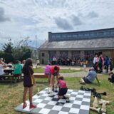 Children play on a large outdoor chess board witha group of performing musicians in the background