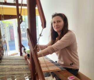 A lady sits at a weaving Loom
