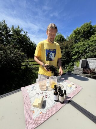 A man stands at a table holding seaweed. The table has ingredients for soap making A man stands at a table holding seaweed. The table has ingredients for soap making