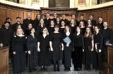 musicians, all dressed in black, stand on a platform, smiling at the camera