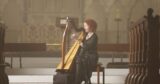 a woman sits, playing a harp